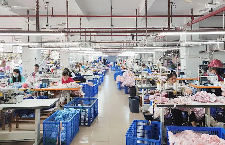 Workers sewing garments across a factory floor with blue sorting bins