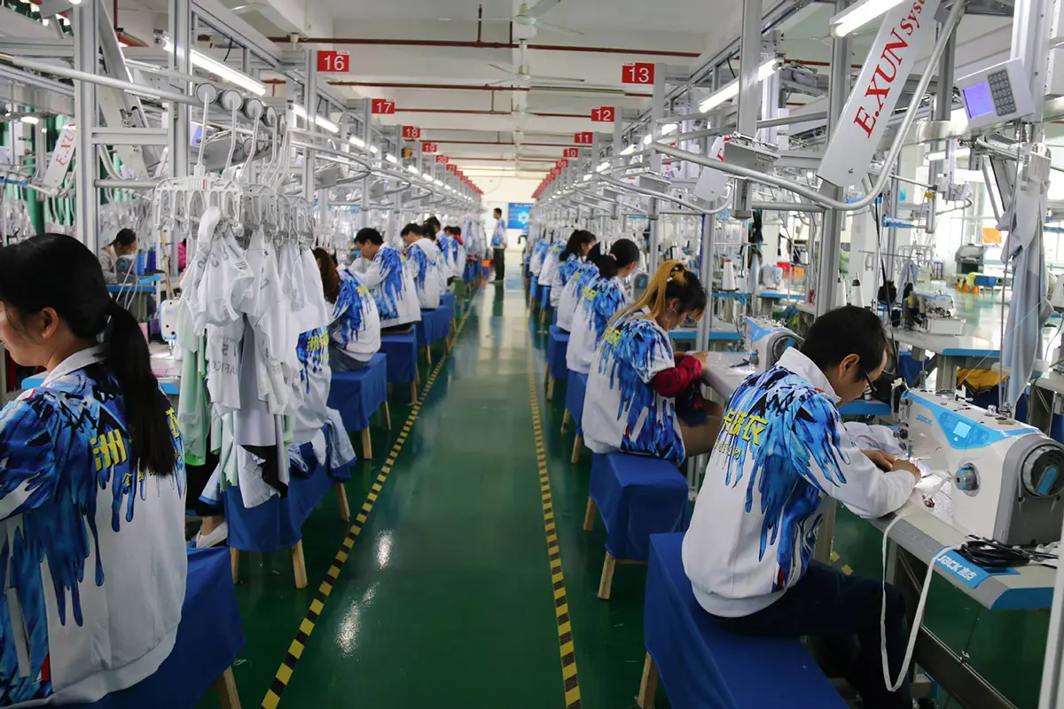 Workers sewing white and blue teamwear at numbered stations