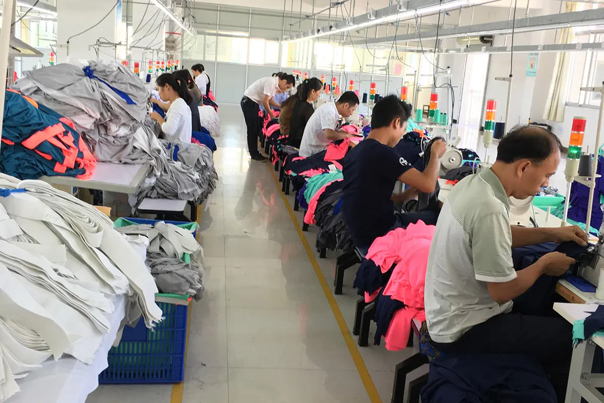 Workers sewing jerseys beside stacks of cut garment pieces