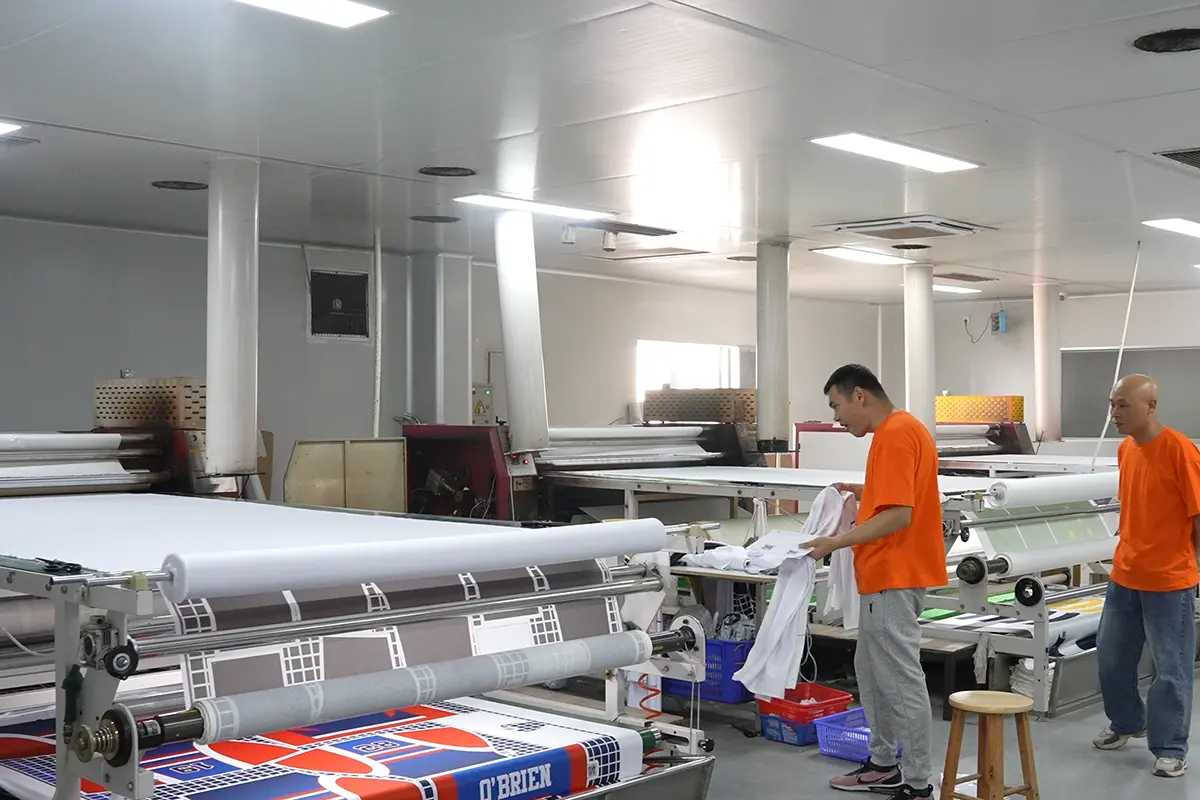 Workers checking printed jersey panels beside a roll heat press