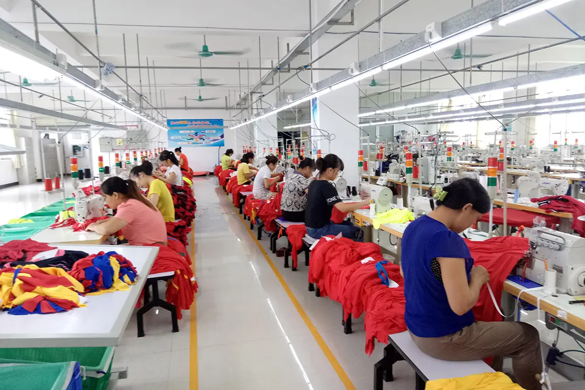 Workers sewing red teamwear along a production line
