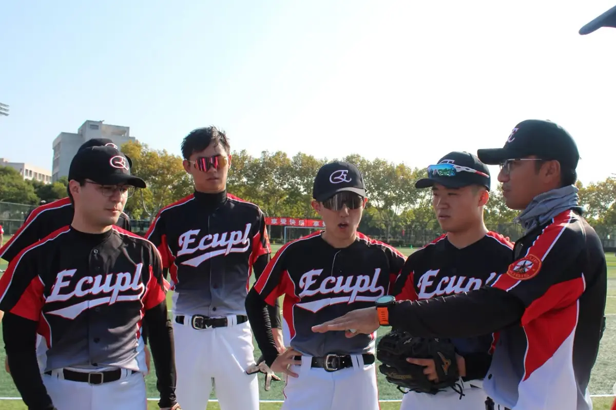 Baseball players in black and red jerseys listening to a coach on the field